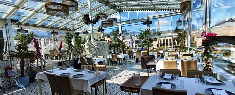 Boşluklu çelik kirişlerle taşınan cam çatının altında masaların bulunduğu salon